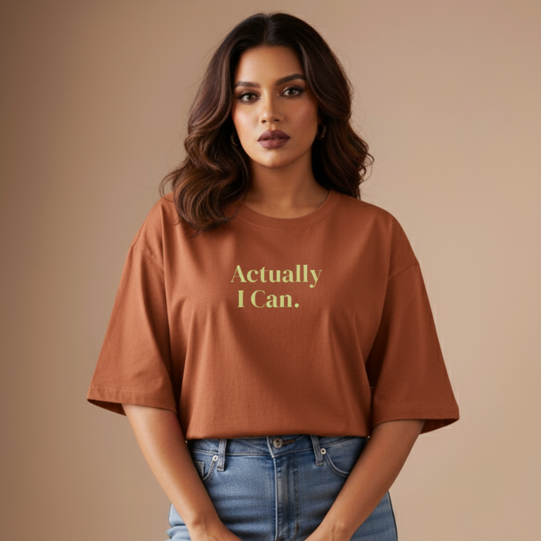 Woman wearing a brown t-shirt with 'Actually I Can.' text on a beige background